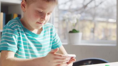 Çocuk Masa 'da ödevini yapıyor. Şirin Çocuk, Akıllı Telefon Cihazı ve Okul Eğitim Kitapları 'nın yardımıyla Evde Öğreniyor. Çalışma ve Eğlence Konsepti .