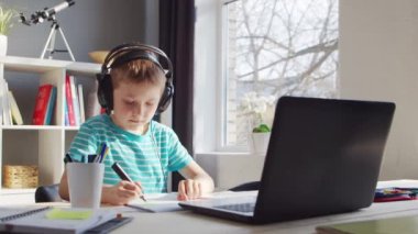 Çocuk Masa 'da ödevini yapıyor. Şirin Çocuk Laptop Bilgisayar ve Okul Ders Kitapları 'nın yardımıyla Evde Öğreniyor. Eğitim ve Uzaktan Eğitim Konsepti.