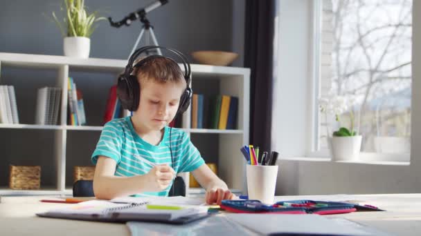 A fiú épp a házi feladatát végzi az asztalnál. Aranyos gyermek tankönyvek és iskolai anyagok segítségével otthon tanul. Tanulmányi és oktatási koncepció. — Stock videók