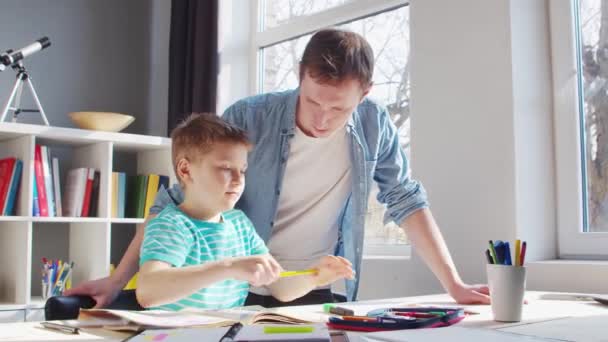 Pojke och far gör läxor vid bordet. Söta barn är att lära sig hemma med hjälp av läroböcker och skolmaterial. Begreppet studier och utbildning. — Stockvideo