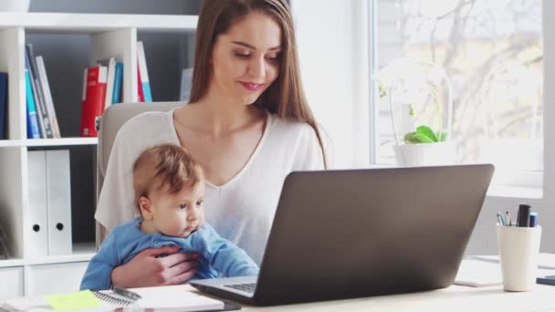Mujer joven Trabaja sentada en casa con su bebé recién nacido. Lugar de trabajo de Emprendedora, Freelancer o Estudiante. Trabajo remoto y concepto de educación. — Vídeos de Stock