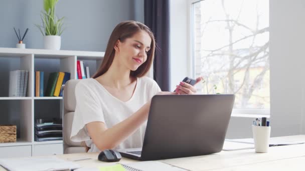 Giovane donna lavora a casa ufficio utilizzando il computer e Smertphone. Luogo di lavoro di imprenditrice, freelance o studentessa. Concetto di lavoro a distanza e istruzione. — Video Stock