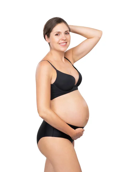 Ung gravid kvinna i svart baddräkt. Flicka väntar ett barn och röra hennes mage isolerad på vit bakgrund. — Stockfoto