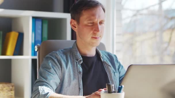 Joven empresario masculino trabaja en la oficina en casa en la computadora. Lugar de trabajo del freelancer o estudiante. Trabajo remoto y concepto de educación. — Vídeos de Stock