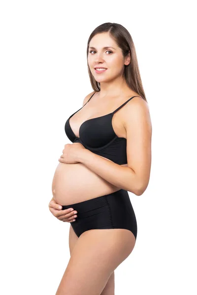 Jeune femme enceinte en maillot de bain noir. Fille attend un bébé et toucher son ventre isolé sur fond blanc. — Photo