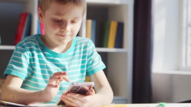 Çocuk Masa 'da ödevini yapıyor. Şirin Çocuk, Akıllı Telefon Cihazı ve Okul Eğitim Kitapları 'nın yardımıyla Evde Öğreniyor. Çalışma ve Eğlence Konsepti .