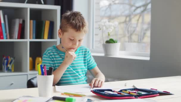 Boy fait ses devoirs à la table. Cute Child apprend à la maison à l'aide de manuels scolaires et de matériel scolaire. Concept d'étude et d'éducation. — Video