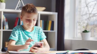Çocuk Masa 'da ödevini yapıyor. Şirin Çocuk, Akıllı Telefon Cihazı ve Okul Eğitim Kitapları 'nın yardımıyla Evde Öğreniyor. Çalışma ve Eğlence Konsepti .