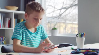 Çocuk Masa 'da ödevini yapıyor. Şirin Çocuk, Akıllı Telefon Cihazı ve Okul Eğitim Kitapları 'nın yardımıyla Evde Öğreniyor. Çalışma ve Eğlence Konsepti .