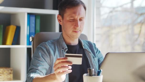 Genç adam internetten kredi kartıyla alışveriş yapıyor. Evde, bilgisayarın başında çalışan kişi. Çevrimiçi alışveriş ve ödeme sistemleri kavramı. — Stok video