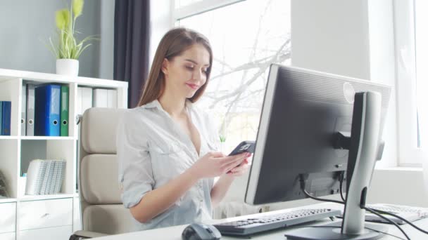 Mladá žena pracuje v kanceláři pomocí počítače a chytrého telefonu. Pracoviště podnikatele, manažera nebo podnikatelky. Koncept vzdálené práce a vzdělávání. — Stock video