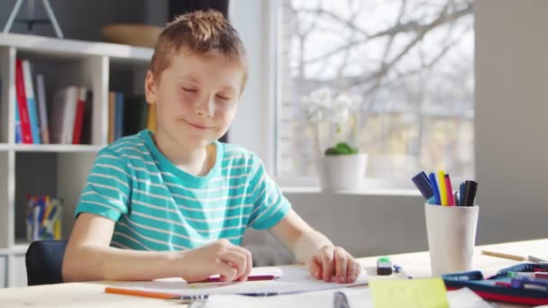 Junge erledigt seine Hausaufgaben am Tisch. Nettes Kind lernt zu Hause mit Hilfe von Lehrbüchern und Schulmaterialien. Studien- und Ausbildungskonzept. — Stockvideo