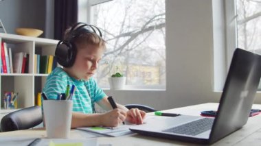 Çocuk Masa 'da ödevini yapıyor. Şirin Çocuk Laptop Bilgisayar ve Okul Ders Kitapları 'nın yardımıyla Evde Öğreniyor. Eğitim ve Uzaktan Eğitim Konsepti.