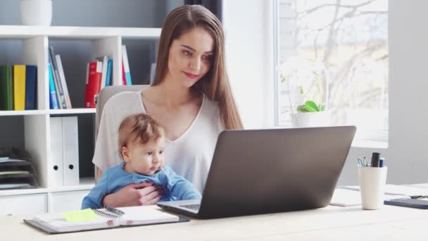 Junge Frau arbeitet, während sie zu Hause mit ihrem neugeborenen Baby sitzt. Arbeitsplatz der Unternehmerin, Freiberuflerin oder Studentin. Fernarbeit und Bildungskonzept. — Stockvideo