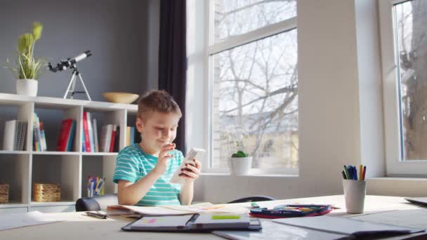 Мальчик делает домашнюю работу за столом. Симпатичный ребенок учится дома с помощью компьютера и школьных учебников. Учиться и развлекаться . — стоковое видео