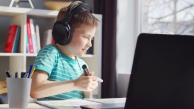 Çocuk Masa 'da ödevini yapıyor. Şirin Çocuk Laptop Bilgisayar ve Okul Ders Kitapları 'nın yardımıyla Evde Öğreniyor. Eğitim ve Uzaktan Eğitim Konsepti.