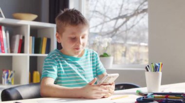 Çocuk Masa 'da ödevini yapıyor. Şirin Çocuk, Akıllı Telefon Cihazı ve Okul Eğitim Kitapları 'nın yardımıyla Evde Öğreniyor. Çalışma ve Eğlence Konsepti .