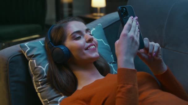 Mujer joven está acostada en casa en el sofá con su dispositivo Gadget Smartphone. Woman is Resting, Chatting and Scrolling Newsfeeds. Inicio Relajación y Concepto de Redes Sociales. — Vídeos de Stock