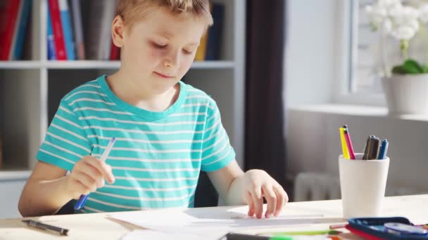 Хлопчик робить домашнє завдання за столом. Мила дитина вчиться вдома за допомогою підручників та шкільних матеріалів. Концепція навчання та освіти . — стокове відео