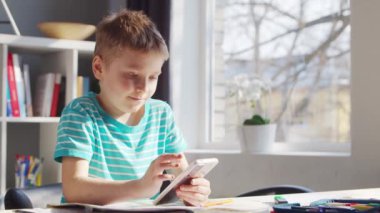 Çocuk Masa 'da ödevini yapıyor. Şirin Çocuk, Akıllı Telefon Cihazı ve Okul Eğitim Kitapları 'nın yardımıyla Evde Öğreniyor. Çalışma ve Eğlence Konsepti .