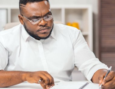 Ofisteki işyerinde. Genç Afro-Amerikalı bir adam bilgisayar ve diğer cihazları kullanarak çalışıyor. Uzak görev konsepti.