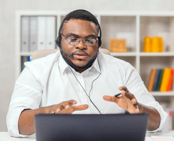 아프리카 계 미국인 남성은 컴퓨터, 헤드셋등의 장치를 사용하여 가정 사무실에서 일한다. 직원들 이 회의 전화를 하고 있어요. 외진 직장. — 스톡 사진