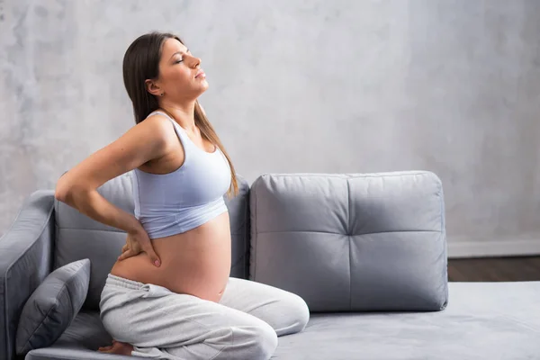 Een jonge zwangere vrouw heeft rugpijn. Zwangerschap, moederschap, gezondheidszorg en levensstijl. — Stockfoto