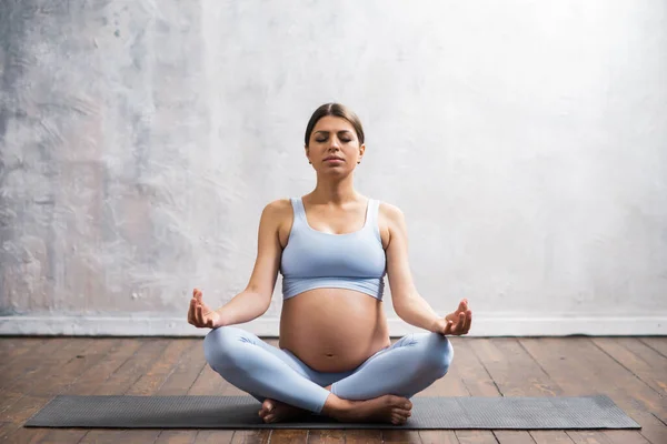 Νεαρή έγκυος γυναίκα που κάνει ασκήσεις γιόγκα και διαλογίζεται στο σπίτι. Υγειονομική περίθαλψη, σύνεση, χαλάρωση και ευεξία. — Φωτογραφία Αρχείου