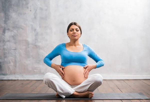 Mujer embarazada joven haciendo ejercicios de yoga y meditando en casa. Atención médica, mindfulness, relajación y concepto de bienestar. —  Fotos de Stock