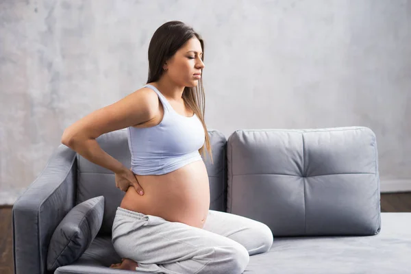 Een jonge zwangere vrouw heeft rugpijn. Zwangerschap, moederschap, gezondheidszorg en levensstijl. — Stockfoto