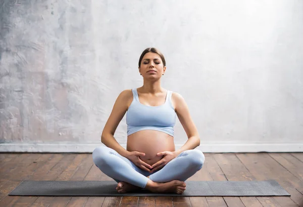 Young pregnant woman doing yoga exercises and meditating at home. Health care, mindfulness, relaxation and wellness concept. — Stock Photo, Image