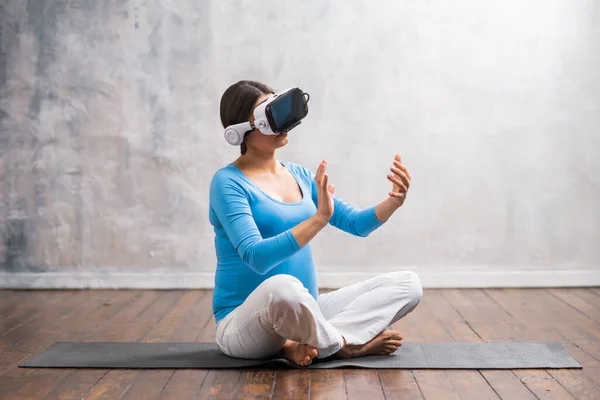 Young pregnant woman in VR helmet. She is preparing for the birth of a child on a virtual simulator at home. Augmented reality technology. — Stock Photo, Image