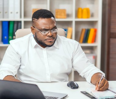 Ofisteki işyerinde. Genç Afro-Amerikalı bir adam bilgisayar ve diğer cihazları kullanarak çalışıyor. Uzak görev konsepti.