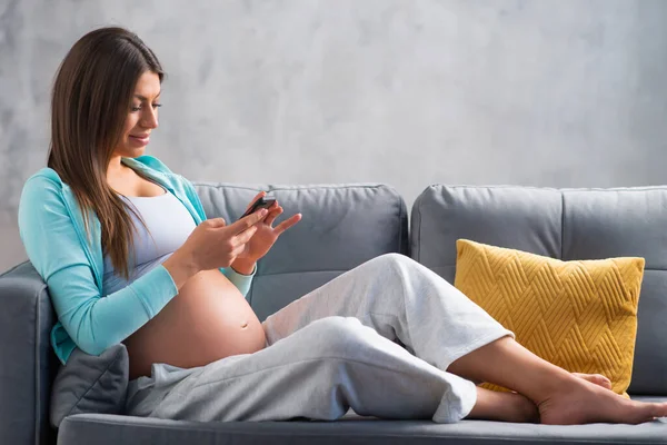 A fiatal terhes nő otthon pihen és gyereket vár. Terhesség, anyaság, egészségügyi ellátás és életmód fogalma. — Stock Fotó