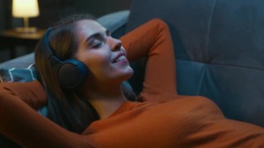 Genç Kadın Gözleri Kapalı Evdeki Koltukta Uzanıyor ve Kulaklıkla Müzik Dinliyor. Kadın Dinleniyor ve İnternetten Radyoyu Dinliyor. Rahatlama, Meditasyon ve Farkındalık.