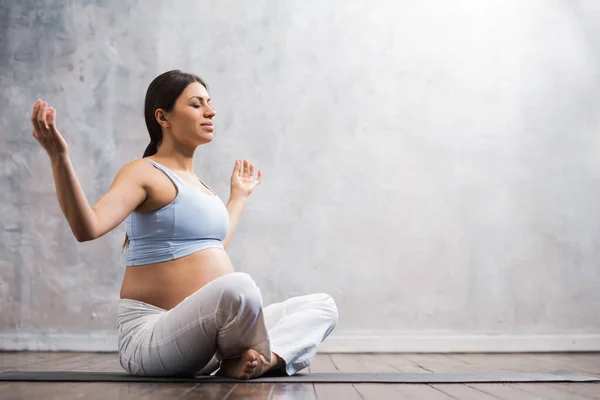 Jovem grávida fazendo exercícios de ioga e meditando em casa. Cuidados de saúde, atenção plena, relaxamento e conceito de bem-estar. — Fotografia de Stock