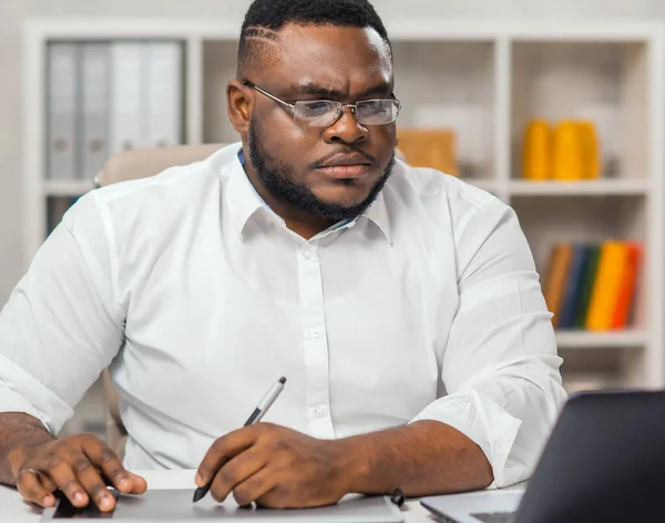 Werkplaats op kantoor. Jonge Afro-Amerikaanse man werkt met een computer, grafische tablet en andere apparaten. Afstandswerkconcept. — Stockfoto