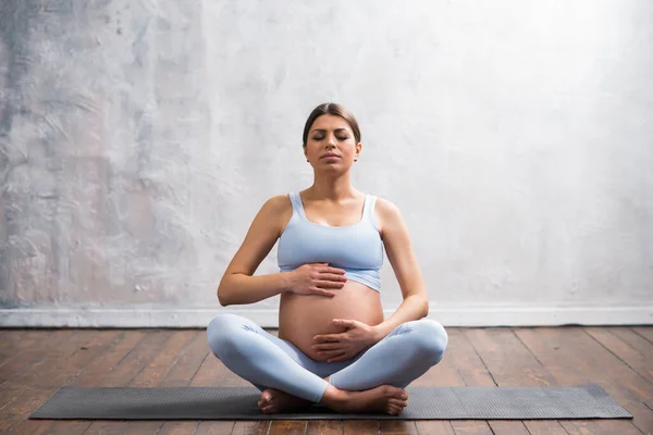 Young pregnant woman doing yoga exercises and meditating at home. Health care, mindfulness, relaxation and wellness concept. — Stock Photo, Image
