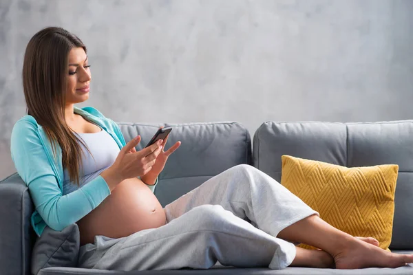 A fiatal terhes nő otthon pihen és gyereket vár. Terhesség, anyaság, egészségügyi ellátás és életmód fogalma. — Stock Fotó