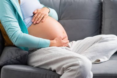 Genç hamile kadın evde dinleniyor ve bebek bekliyor. Hamilelik, annelik, sağlık ve yaşam tarzı kavramı.