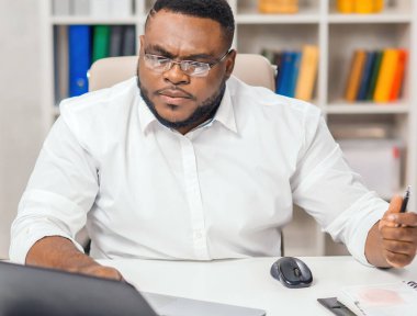 Ofisteki işyerinde. Genç Afro-Amerikalı bir adam bilgisayar ve diğer cihazları kullanarak çalışıyor. Uzak görev konsepti.