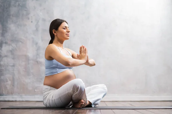 Young pregnant woman doing yoga exercises and meditating at home. Health care, mindfulness, relaxation and wellness concept. — Stock Photo, Image