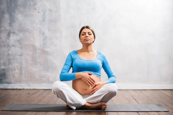 Young pregnant woman doing yoga exercises and meditating at home. Health care, mindfulness, relaxation and wellness concept. — Stock Photo, Image