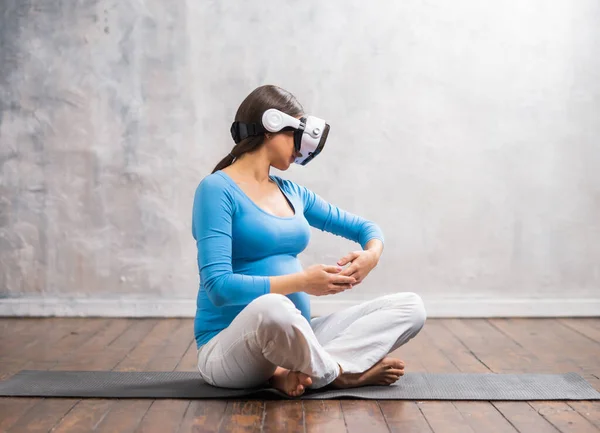 Young pregnant woman in VR helmet. She is preparing for the birth of a child on a virtual simulator at home. Augmented reality technology. — Stock Photo, Image