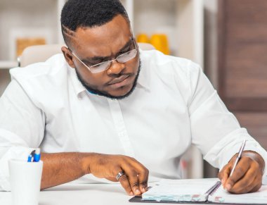 Ofisteki işyerinde. Genç Afro-Amerikalı bir adam bilgisayar ve diğer cihazları kullanarak çalışıyor. Uzak görev konsepti.