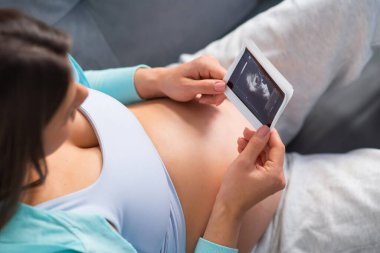 Genç hamile kadın evde dinleniyor ve bebek bekliyor. Hamilelik, annelik, sağlık ve yaşam tarzı kavramı.