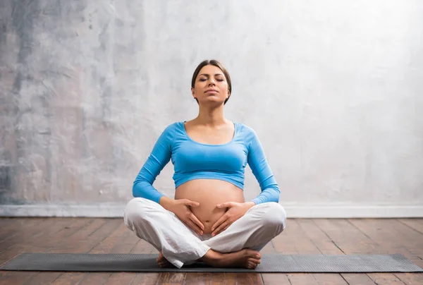 Young pregnant woman doing yoga exercises and meditating at home. Health care, mindfulness, relaxation and wellness concept. — Stock Photo, Image