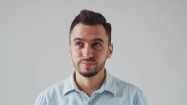 Young Caucasian Brunet Man is Looking at the Camera on a Light Gray Background. Studio Male Face Portrait. Natural Day Light.
