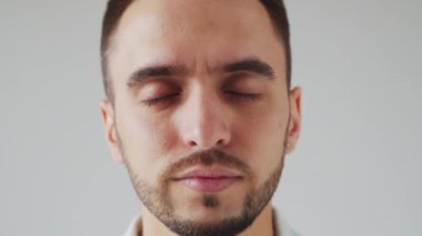 Genç Kafkasyalı Brunet Adam Açık Gri Arkaplanda Kameraya Bakıyor. Stüdyo Erkek Yüz Portresi. Doğal Gün Işığı.