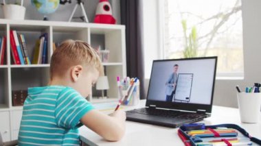 Çocuk Masa 'da ödevini yapıyor. Şirin Çocuk Laptop Bilgisayar ve Okul Ders Kitapları 'nın yardımıyla Evde Öğreniyor. Eğitim ve Uzaktan Eğitim Konsepti.
